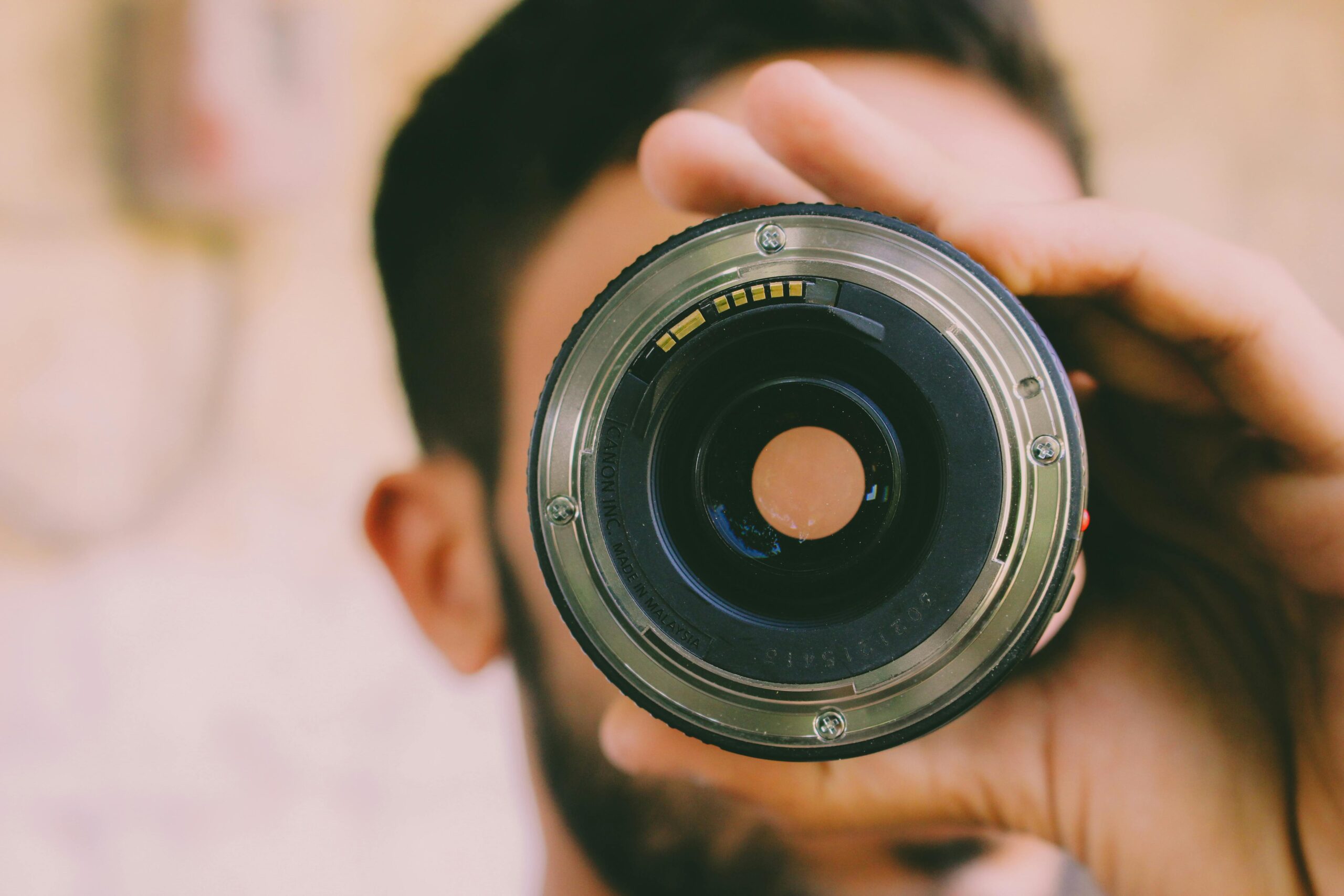 A man holding a camera lens close to his eye, focusing on photography.