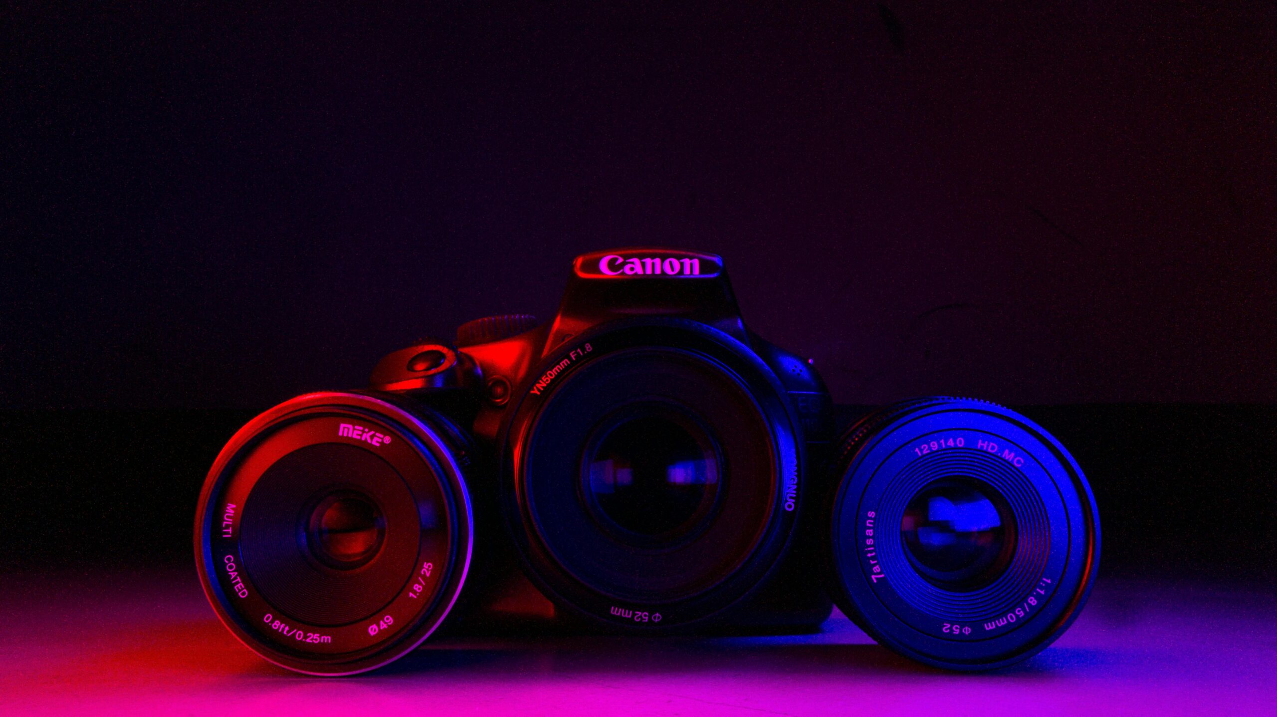 A DSLR camera with lenses creatively lit by vibrant neon lights on a dark background.